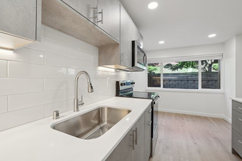 A modern kitchen with a stainless steel sink and white countertops.